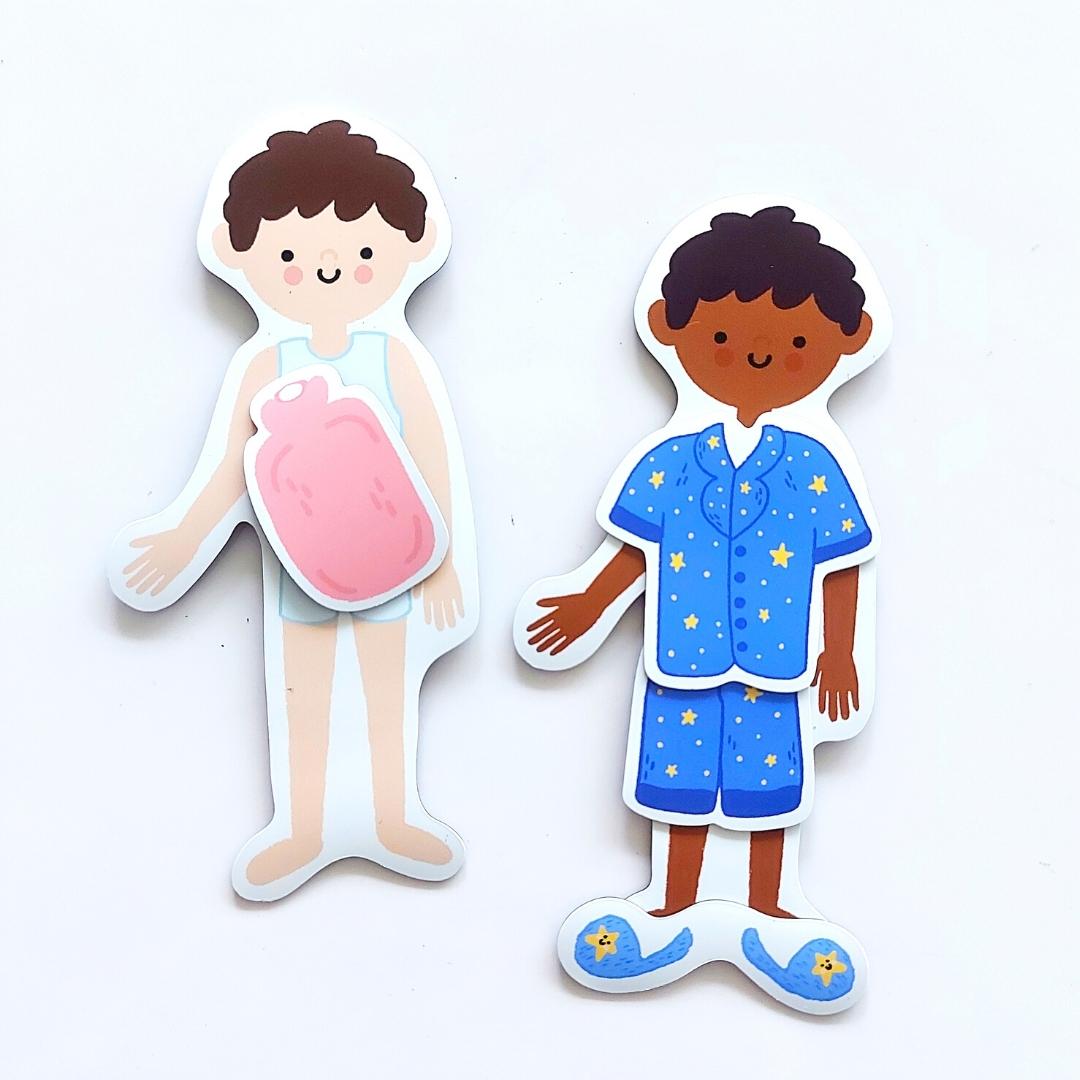 2 child magnet pieces are shown against a white background. One is dressed in blue star pyjamas with slippers, the other is in underclothes with a hot water bottle against their stomach.