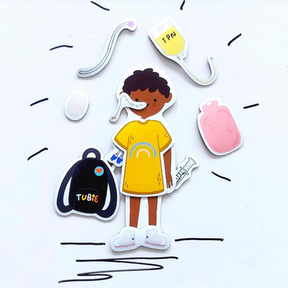The child magnet is dressed in a happy yellow rainbow dress and white sneakers. They have an NG tube installed, a PICC line and are holding a syringe and Tubie backpack. Around them is a hot water bottle, TPN bag, tube extension, and ostomy pouch.